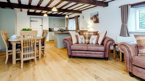 A cozy living room with a wooden ceiling, a dining area with a table and chairs, a sofa with decorative pillows, and a kitchen in the background. - The Old Granary - UK12135 (Hewelsfield, near Lydney)