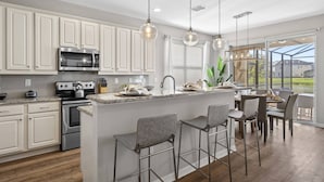 A modern kitchen with white cabinets, stainless steel appliances, and a large island with bar stools. - Veranda Palms 8 Bedroom Home with Pool(2208) (Kissimmee)