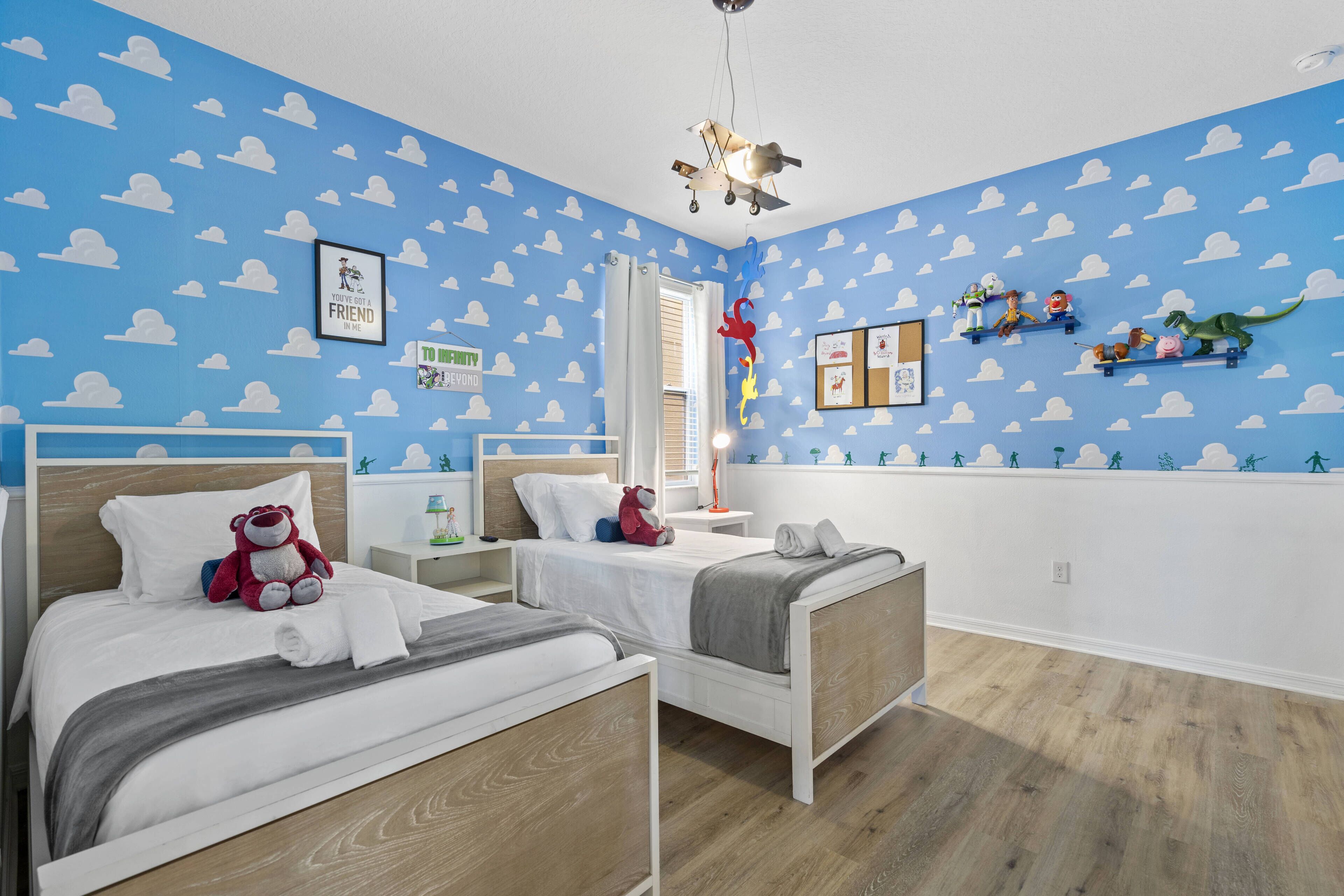 A bedroom with two beds, a window with curtains, a ceiling fan, and wall decorations including a framed picture and a shelf with toys.