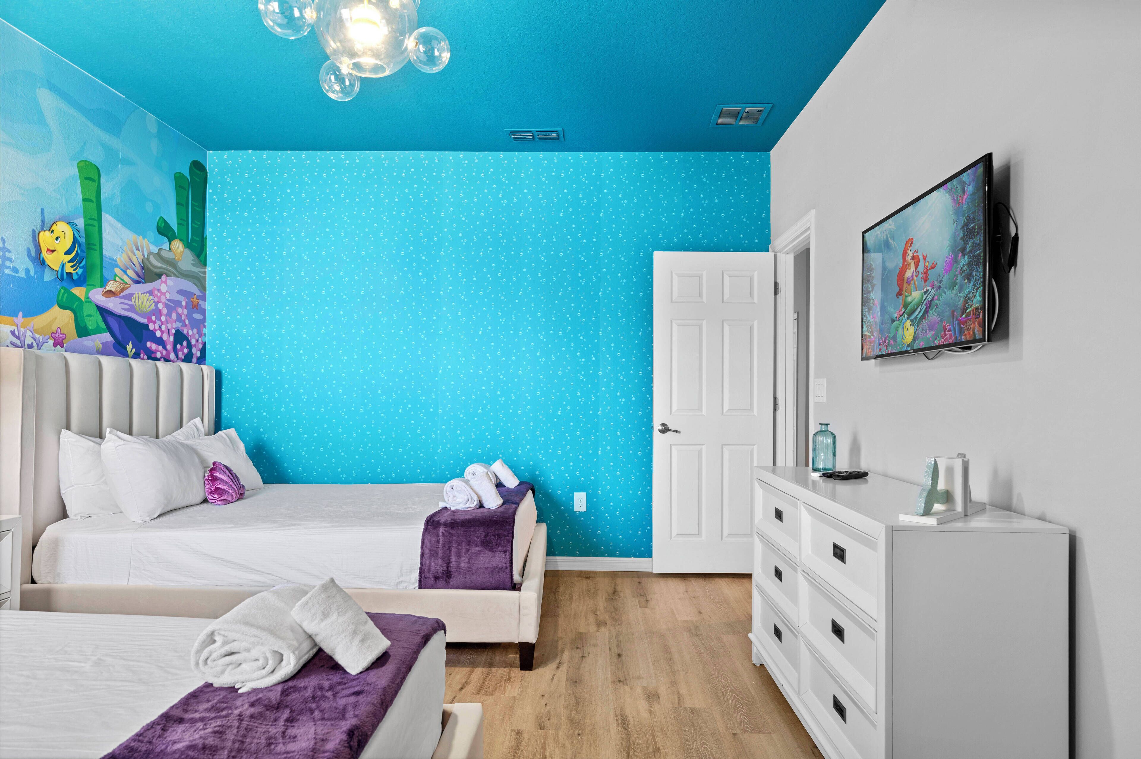 A hotel room with a large bed, a dresser, a television, and a mural on the wall.