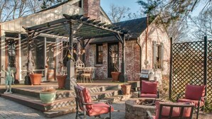 Un patio con mobiliario exterior, una pérgola y un edificio de ladrillo con chimenea.