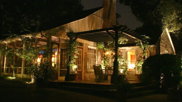 Un espacio al aire libre cubierto con chimenea de ladrillo, pérgola de madera y plantas en macetas.