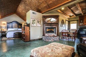 A spacious room with a large bed, a fireplace, and a dining area.