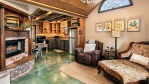 Una sala de estar acogedora con chimenea, sofá de cuero y un comedor con alacenas de madera y refrigerador.