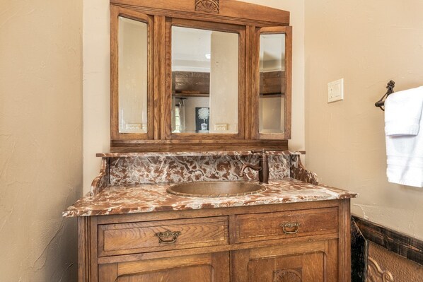 Un baño con tocador de madera, encimera de mármol y espejo sobre el lavabo.