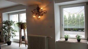 Une pièce avec un radiateur, un luminaire fixé au mur et des plantes en pot près des fenêtres.