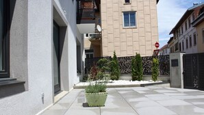 Un bâtiment moderne doté d’une cour dallée, d’un jardinier et d’un portail.