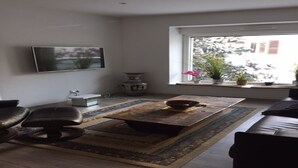 Un salon comprenant un canapé, une table basse, un téléviseur fixé au mur et une fenêtre agrémentée de plantes.