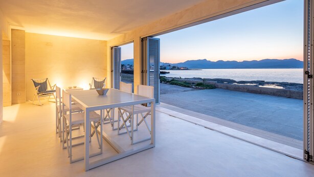 A modern interior with a dining area, a rocking chair, and a view of the sea at sunset. - MOREMAR - A Special House by the Sea (Alcudia)