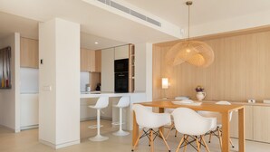 A modern kitchen with white cabinetry, a wooden dining table, and white bar stools. - MOREMAR - A Special House by the Sea (Alcudia)