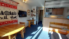 A cozy room with a wooden dining table, a TV mounted on the wall, a microwave, and a small kitchen area.