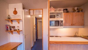 Pieni, käytännöllinen keittiö, jossa on puiset kaapit, mikroaaltouuni ja pesuallas. Keittiössä on myös puinen hylly, jossa on kirjoja ja pullo. Käytävältä pääsee toiseen huoneeseen.