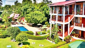 A multi-story building with a pool, surrounded by lush greenery and a clear sky. - Divisamar Manuel Antonio, A natural paradise for you. (Quepos)
