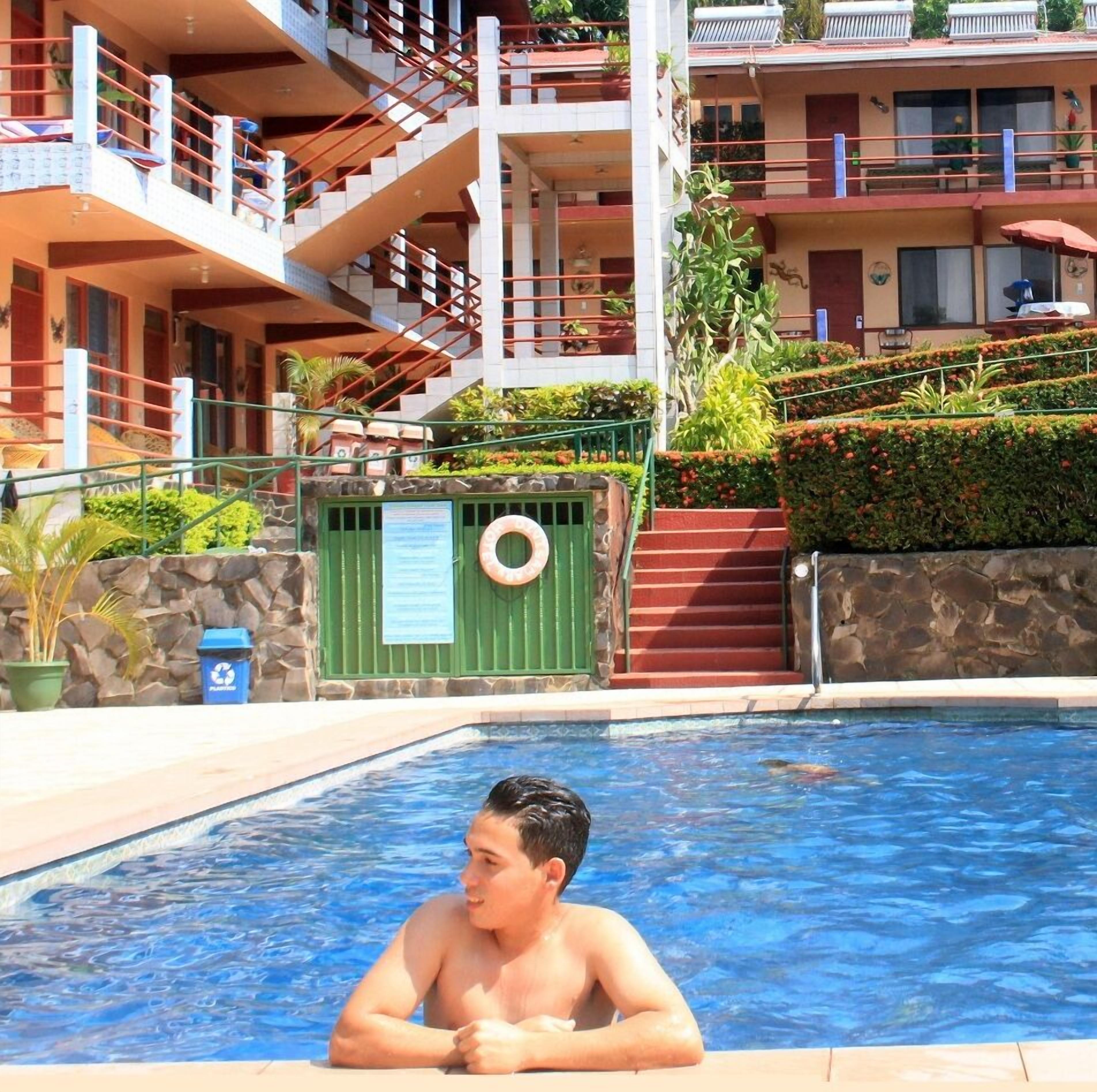 Una piscina con una persona che si rilassa nell'acqua, circondata da un muro di pietra e vegetazione.