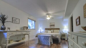 Een slaapkamer met een bed, nachtkastjes, een dressoir, een raam en een plafondventilator.