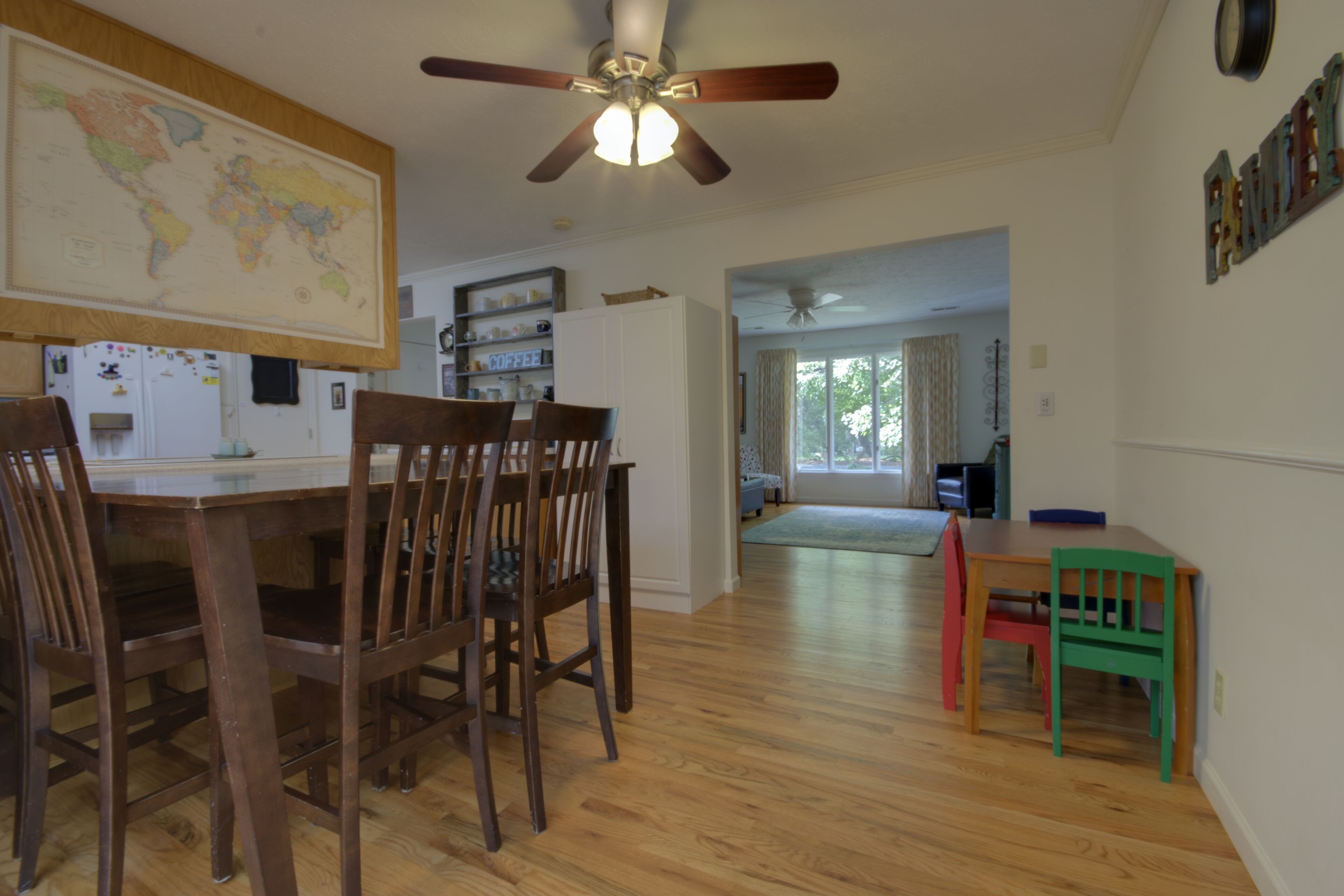 A dining area with wooden chairs and a table, a ceiling fan, and a world map on the wall.