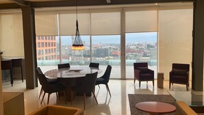 A spacious living area with a round table and chairs, a sofa, and a coffee table. Large windows offer a city view. - PH CIELO ALAMEDA, JUAREZ 52 (Centro)