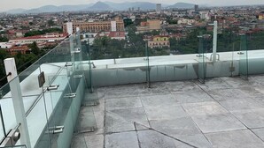 A rooftop terrace with glass railings, offering a panoramic view of a cityscape with buildings and mountains in the distance. - PH CIELO ALAMEDA, JUAREZ 52 (Centro)