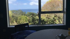 A room with a large window overlooking a lush landscape and the ocean. - Looking out over the ocean with uninterrupted views to Mayor Island and beyond! (Onemana)