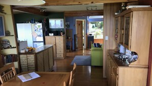 A spacious kitchen with wooden cabinets, a dining table with chairs, and a view of the backyard. - Looking out over the ocean with uninterrupted views to Mayor Island and beyond! (Onemana)