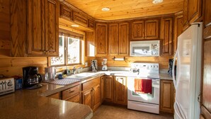 A wooden cabin kitchen with a stove, refrigerator, and wooden cabinets. - Enjoy the spectacular views from the balcony and cabin at this mountain location (Julian)