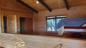 A cabin interior with a wooden ceiling, a window with a view of trees, a bunk bed, and a staircase. - Enjoy the spectacular views from the balcony and cabin at this mountain location (Julian)