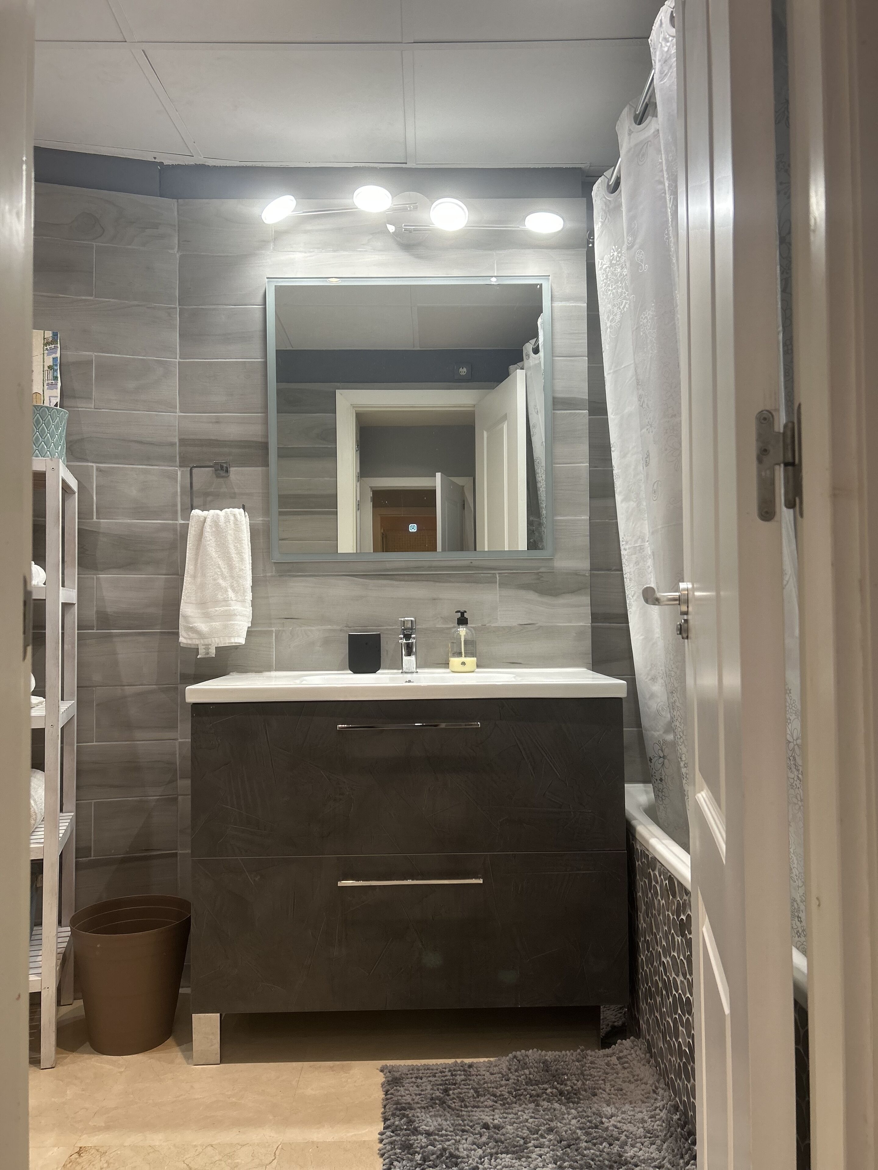 A modern bathroom with a dark vanity, a large mirror, and a shower curtain.