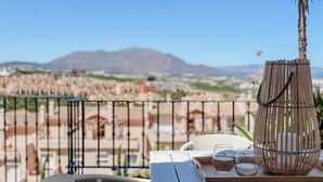 A terrace with a white table and wicker chairs, a small plant, and a view of a cityscape with mountains in the background. - Sun-Soaked Penthouse w/ 3 Terraces • Walk to Beach, Port & Dining • Sleeps 6 (Manilva)