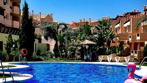 A swimming pool with clear blue water, surrounded by palm trees and a row of buildings with balconies. - Sun-Soaked Penthouse w/ 3 Terraces • Walk to Beach, Port & Dining • Sleeps 6 (Manilva)