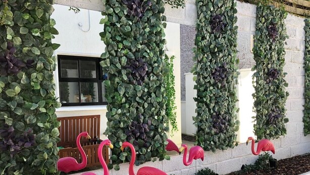 A building facade with vertical gardens and pink flamingo statues.