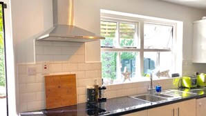 A modern kitchen with a black countertop, white cabinets, a stainless steel range hood, and a window with a view of greenery.