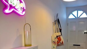 A hallway with a neon sign, a white cabinet, a door with a window, and a bag hanging on the wall.
