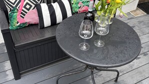A black metal table with a vase of tulips and two wine glasses on a wooden deck.