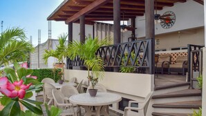 Un patio al aire libre con una mesa redonda y sillas, rodeado de plantas en macetas y una escalera que lleva a un nivel superior.