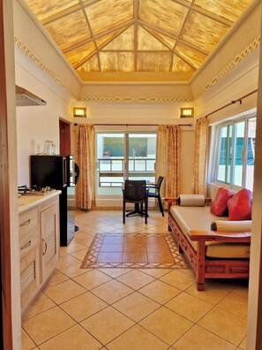 Una habitación con suelo de baldosas, un sofá con cojines rojos, una mesa de comedor con sillas, un televisor y una ventana con cortinas.