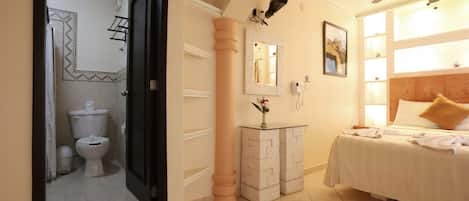 A hotel room with a bed, a bathroom with a toilet, a mirror, and a ceiling fan.