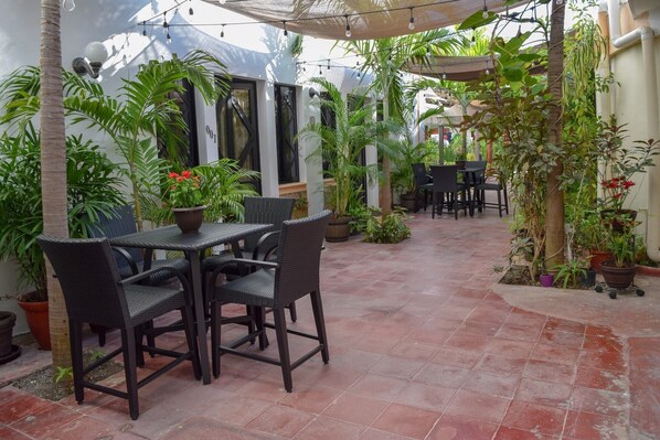 Un patio con mesa y sillas, rodeado de plantas en macetas y una pérgola.