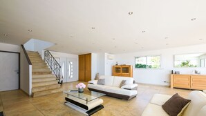 A spacious living area with a staircase, a glass coffee table, a white sofa, and a wooden cabinet.