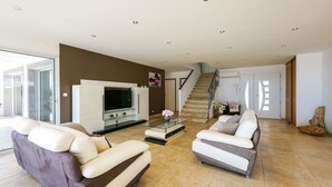 A modern living room with a sofa, a coffee table, and a TV. There is a staircase leading to another level.