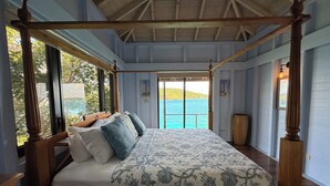 A four-poster bed with a floral bedspread, large windows, and a view of the sea. - Great House Villa, Jost Van Dyke (Jost Van Dyke)