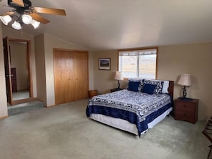 A bedroom with a bed, two bedside tables, a ceiling fan, a window, and a door.
