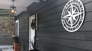 Una casa moderna con fachada de madera oscura, un letrero con una brújula en la pared y dos macetas de madera con plantas.