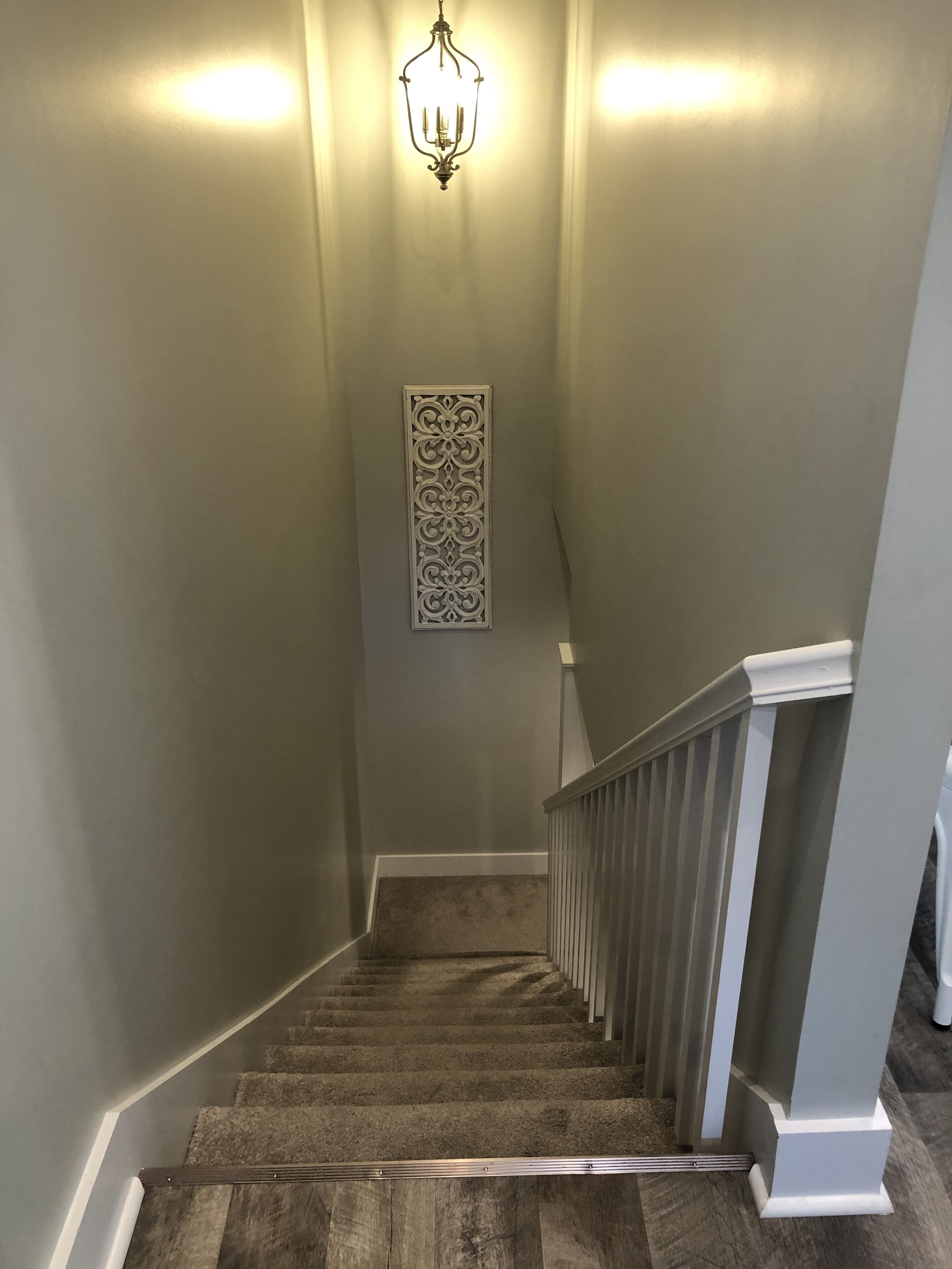 A staircase with a wooden handrail, a light fixture, and a decorative panel on the wall.