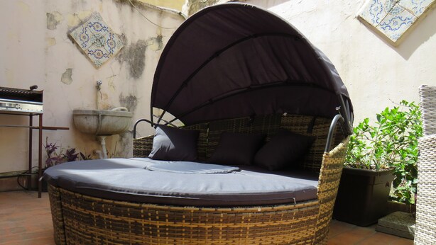 Un letto circolare in vimini con tenda, una pianta in vaso e un pavimento piastrellato.