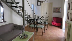 Un soggiorno con una scala, una zona pranzo con sedie e un tavolo, un divano rosso e un termosifone.
