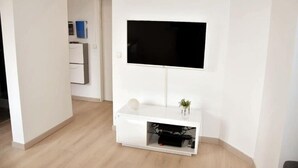 A modern living room with a flat-screen TV mounted on the wall, a white entertainment unit below, and a wooden floor. - Beautiful apartment located in the Louvre-Bollaert district (Lens)