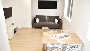 A modern living room with a grey sofa, a wooden dining table with white chairs, and a small round side table. - Beautiful apartment located in the Louvre-Bollaert district (Lens)