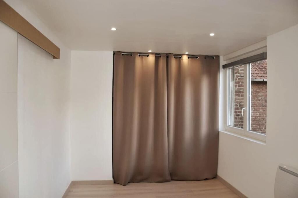 Una habitación con un ventanal grande, una cortina y piso de madera.
