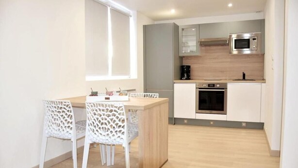 A modern kitchen with a built-in oven, microwave, and coffee maker. There is a wooden dining table with two white chairs. - Beautiful apartment located in the Louvre-Bollaert district (Lens)