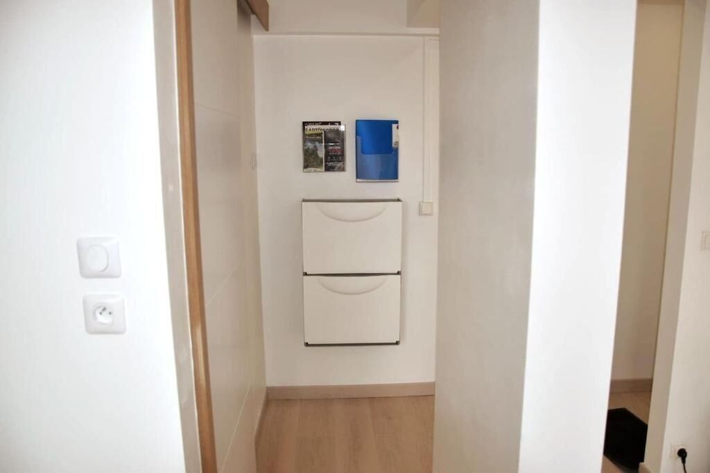 Un couloir étroit avec une porte blanche, un meuble blanc fixé au mur et un dossier bleu accroché au mur.